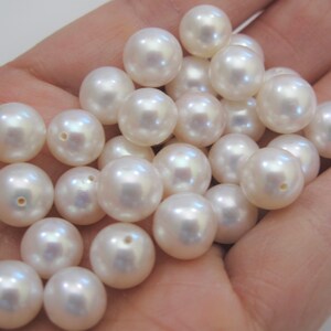 May include: A collection of white round pearls, some with iridescent sheen, in a hand.