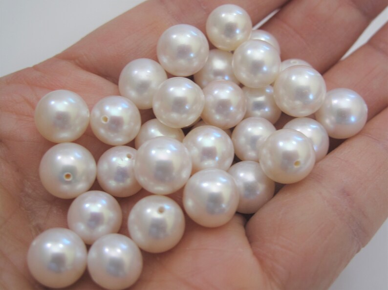 May include: A collection of white round pearls, some with iridescent sheen, in a hand.