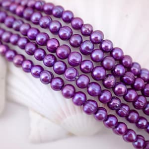 May include: A strand of purple freshwater pearls. The pearls are round and have a slight iridescent sheen.
