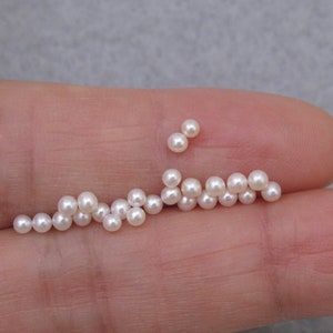 May include: A collection of white pearls of varying sizes, arranged in a line on a finger.