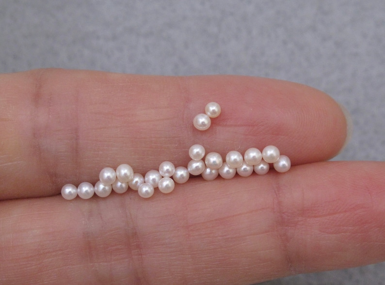 May include: A collection of white pearls of varying sizes, arranged in a line on a finger.