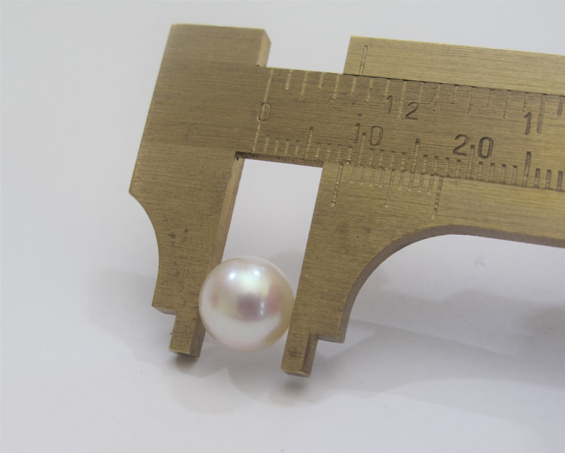 May include: A white pearl measuring approximately 1.2 cm in diameter, being measured with a caliper.