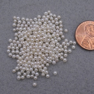 May include: A pile of small, white pearl beads, about the size of a US penny.