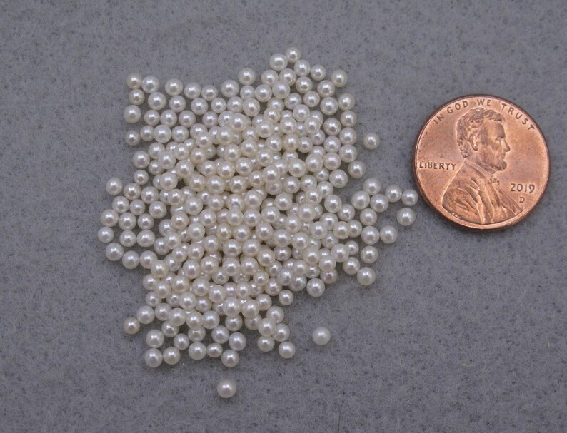 May include: A pile of small, white pearl beads, about the size of a US penny.