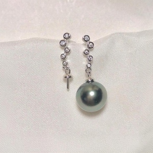 Könnte beinhalten: Ein Paar silberne Ohrringe mit je einem schwarzen Perlen-Tropfen. Die Ohrringe haben eine silberne Kette mit kleinen, klaren Steinen.