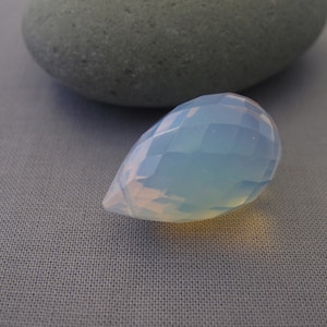 May include: A teardrop-shaped, faceted, light blue opal gemstone.