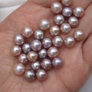 May include: A collection of round, iridescent pearls in shades of lavender and pink. The pearls are smooth and have a subtle sheen.
