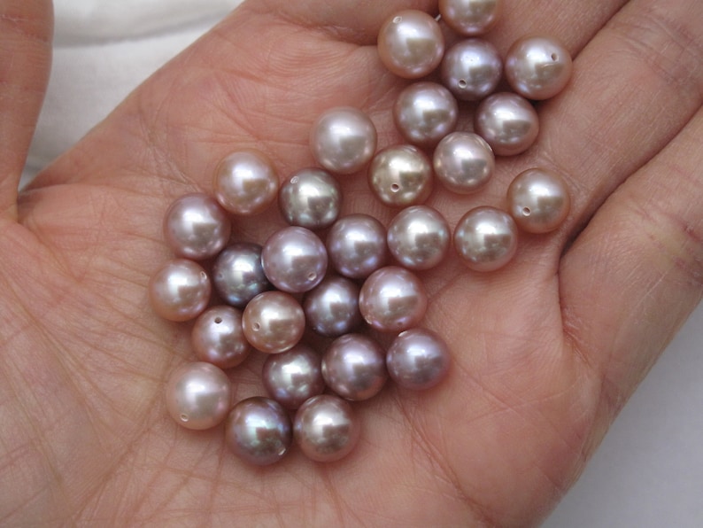 May include: A collection of round, iridescent pearls in shades of lavender and pink. The pearls are smooth and have a subtle sheen.