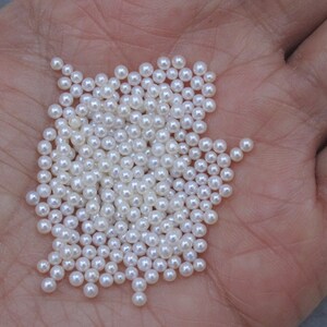 May include: A pile of small, white, round pearls in a person's hand.