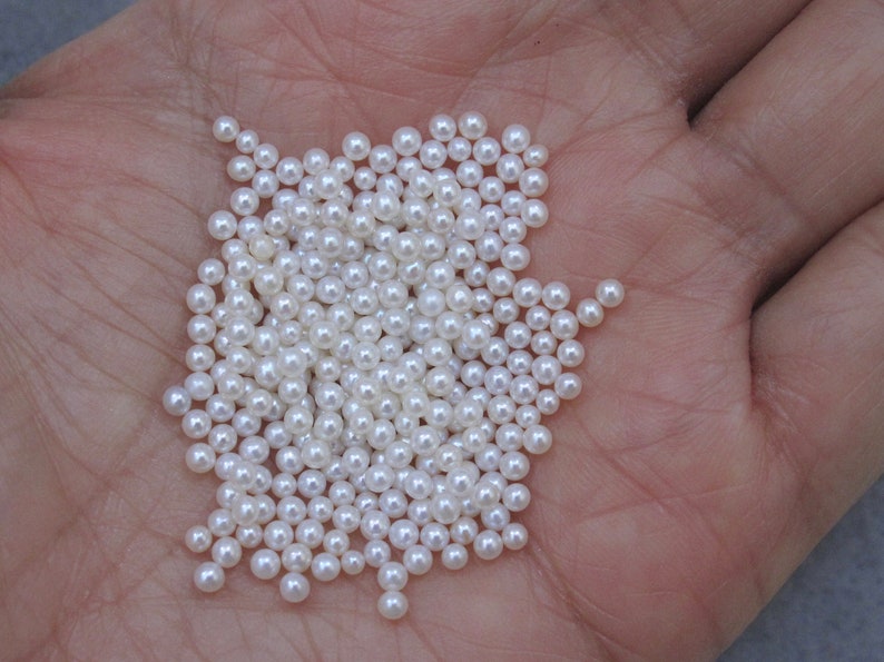 May include: A pile of small, white, round pearls in a person's hand.