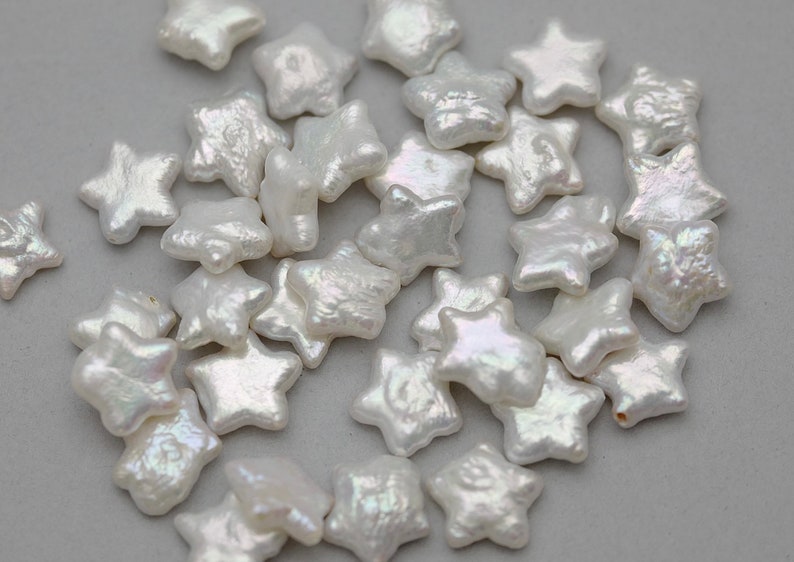 May include: A collection of white pearl star-shaped beads. The beads are iridescent and have a slightly irregular shape.
