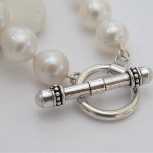 May include: A white pearl bracelet with a silver toggle clasp. The pearls are large and round, and the clasp is decorated with small beads.