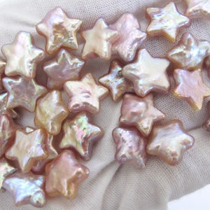 May include: A collection of iridescent pink star-shaped pearl beads. The beads are arranged in a loose pile on a white surface.
