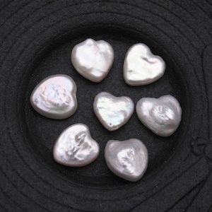 May include: Seven white heart-shaped pearl beads on a black background.