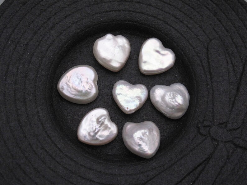 May include: Seven white heart-shaped pearl beads on a black background.