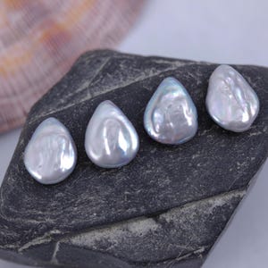 May include: Four iridescent white baroque pearls with a teardrop shape, displayed on a dark gray rock.