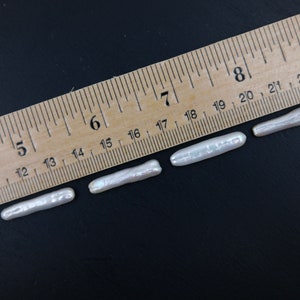 Puede incluir: Cuatro perlas keshi blancas de diferentes longitudes, medidas con una regla de madera con marcas en pulgadas. Las perlas var&iacute;an en tama&ntilde;o de 3,8 cm a 6,4 cm.