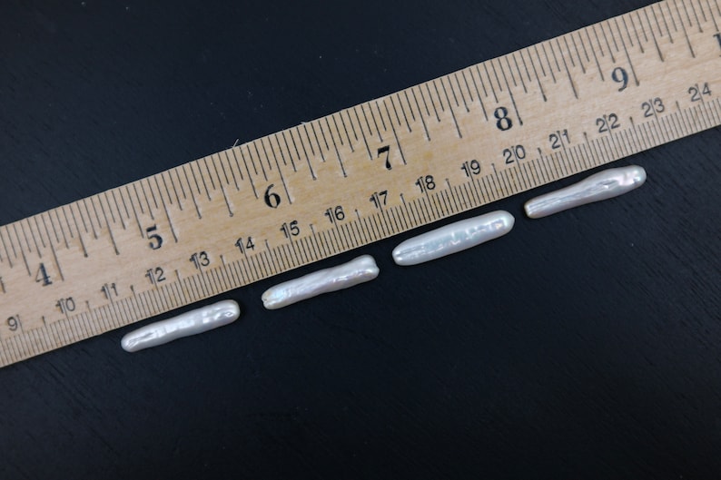 Puede incluir: Cuatro perlas keshi blancas de diferentes longitudes, medidas con una regla de madera con marcas en pulgadas. Las perlas var&iacute;an en tama&ntilde;o de 3,8 cm a 6,4 cm.