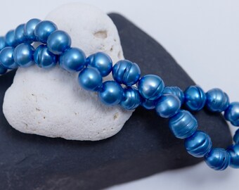 Puede incluir: Una hebra de cuentas de perlas azules sobre un fondo de piedra blanca y gris.