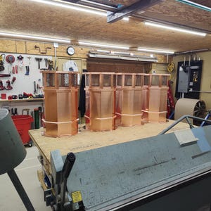 May include: Four copper chimney caps with mesh screens on top, sitting on a wooden surface in a workshop.