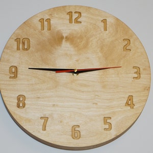 May include: A round wooden clock with black and red hands. The clock face is made of light wood with the numbers 1 through 12 printed in a dark color.