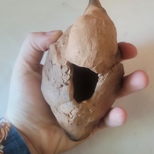 May include: A small, hand-crafted clay birdhouse with a rounded roof and a hole for entry. The birdhouse is made of brown clay and has a rustic, textured surface.