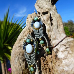 Peut inclure: Boucles d'oreilles en macramé gris avec des perles turquoise et bleues et un pendentif en pierre blanche. Les boucles d'oreilles sont suspendues à un morceau de bois flotté.