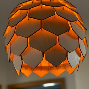 Könnte beinhalten: Eine hölzerne Pendelleuchte mit einem Wabenmuster. Das Licht ist eingeschaltet und strahlt ein warmes orangefarbenes Licht aus.