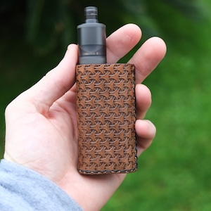 May include: A brown leather case with a geometric pattern, designed to hold a vape mod. The case has a dark brown stitching around the edges.