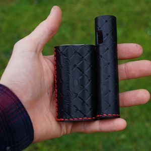May include: Black leather case with red stitching for an electronic cigarette. The case has a quilted pattern and the text "Smok" is embossed on the front.