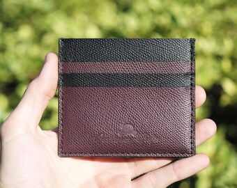 May include: A burgundy leather card holder with black stripes and a subtle embossed logo.