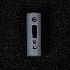 Può includere: Un mod vape cilindrico grigio con una finitura testurizzata e tre pulsanti argentati.