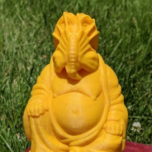 Puede incluir: Una figurita de Buda sonriente de color amarillo impresa en 3D con cabeza de langosta.