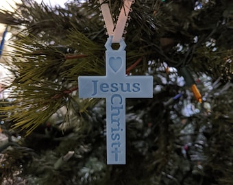 May include: A light blue cross-shaped Christmas ornament with a heart at the top and the words "Jesus Christ" written vertically on the cross.