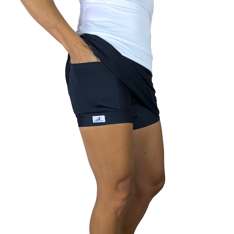 May include: Black athletic skirt with a built-in short and a single pocket on the right side. The skirt has a small white label with the text "Dress Down" in blue.