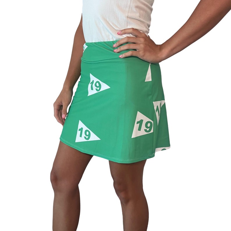 Puede incluir: Una falda verde con parches blancos en forma de tri&aacute;ngulo que tienen el n&uacute;mero "19" impreso en ellos.