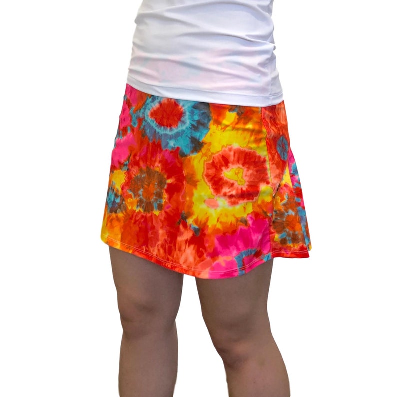 May include: A colorful tie-dye skirt with a bright orange, yellow, pink, and blue pattern. The skirt is made of a soft, stretchy fabric and has a comfortable fit.