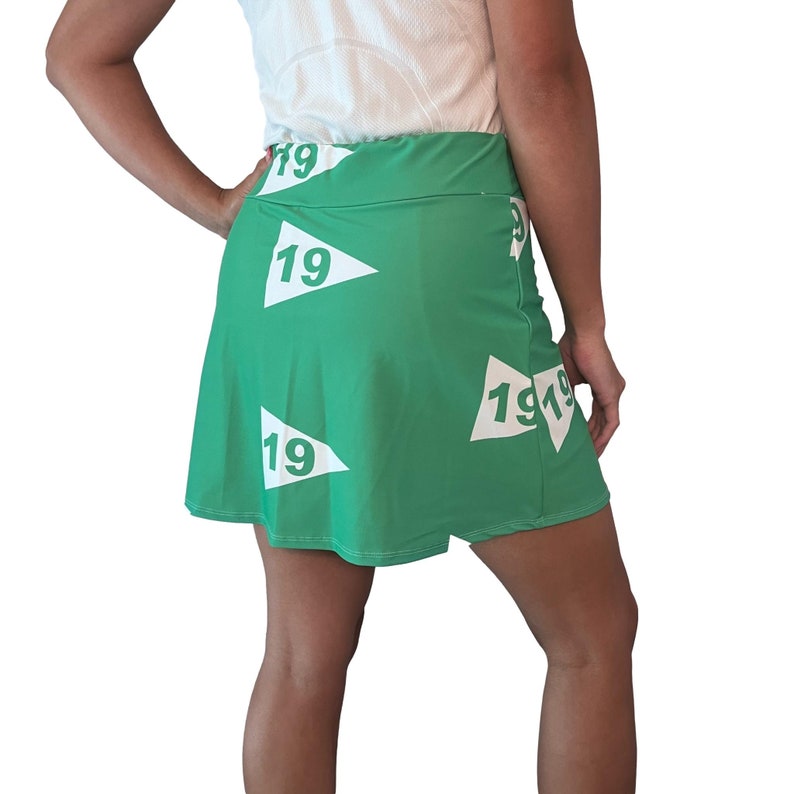 Puede incluir: Una falda verde con banderas blancas impresas en ella. Cada bandera tiene el n&uacute;mero "19" impreso en ella.