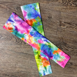 Könnte beinhalten: Ein Paar bunte Armwärmer im Tie-Dye-Muster. Die Armwärmer sind aus dehnbarem Stoff gefertigt und haben ein lebendiges Tie-Dye-Muster in den Farben Pink, Blau, Grün und Orange.