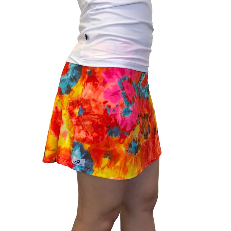 May include: A colorful tie-dye skirt with a bright orange, yellow, pink, and blue pattern. The skirt has a ruffled hem and a small logo on the side.
