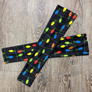 May include: A pair of black arm warmers with a repeating pattern of colorful light bulbs. The arm warmers are made of a soft, stretchy fabric.