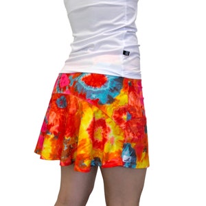 May include: A colorful tie-dye skirt with a bright orange, yellow, pink, and blue pattern. The skirt has a flared silhouette and a small pocket on the right side.