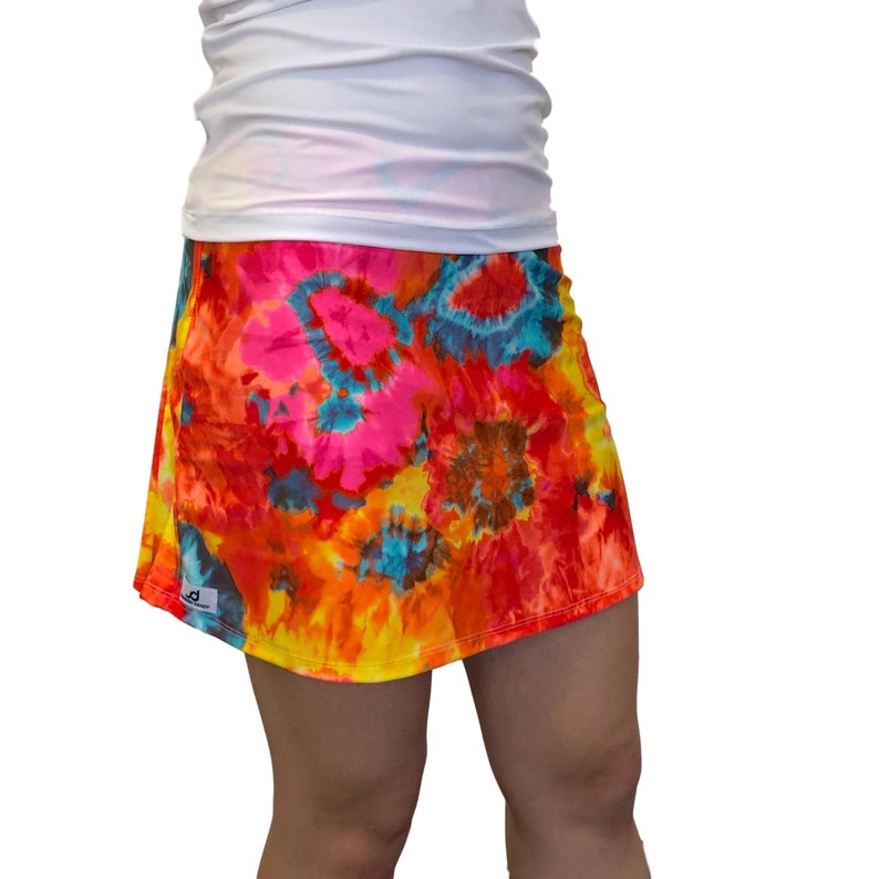 May include: A colorful tie-dye skirt with a bright orange, yellow, pink, blue, and brown pattern. The skirt is made of a soft, stretchy fabric and has a comfortable fit.