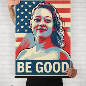 May include: Poster with a portrait of a woman against a backdrop of the American flag. The poster has the words "BE GOOD" in large letters. The website "woke-wear.com" is visible at the top.