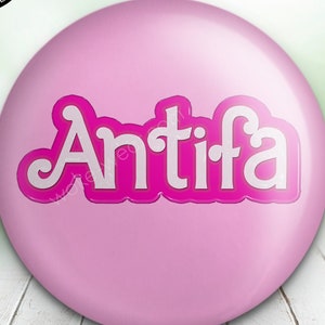 May include: Pink button badge with the word "Antifa" in white letters with a pink outline.