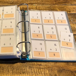 May include: A binder with clear plastic pockets containing flashcards for math problems. The flashcards have white backgrounds with black numbers and symbols. The flashcards are labeled with numbers from 1 to 18 and include addition and division problems.