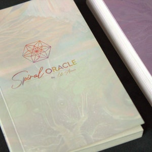 Może przedstawiać: Biała i tęczowa książka z geometrycznym wzorem i tekstem "Spiral Oracle by Lisa A."