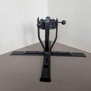 Peut inclure: Un support de sapin de Noël en métal noir doté d'une base en croix avec quatre pieds plats. Le support cylindrique central présente une surface texturée et comprend deux tiges horizontales réglables avec des extrémités sphériques pour fixer le tronc.