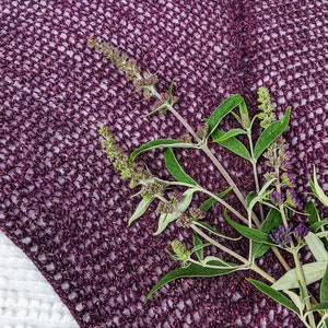 May include: Purple crocheted fabric with a sprig of green leaves and purple flowers.