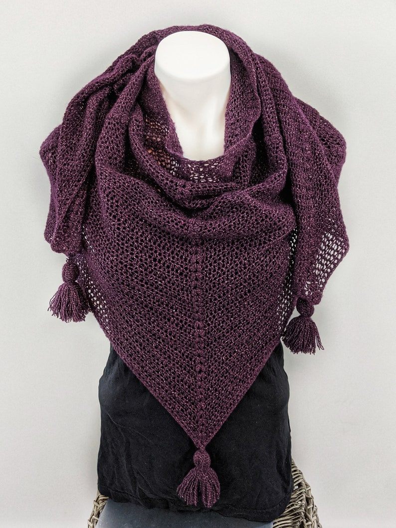 May include: A purple knitted shawl with a sparkly finish and three tassels. The shawl is draped over a mannequin.